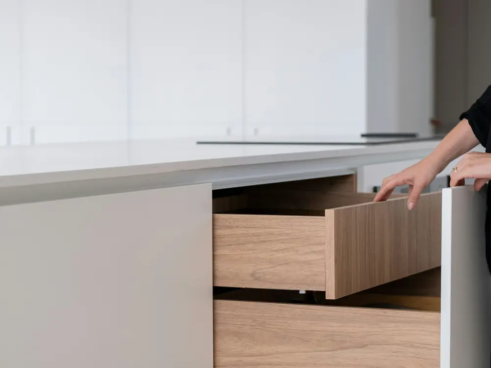 Hand pulling open a wide kitchen drawer in a white cabinet