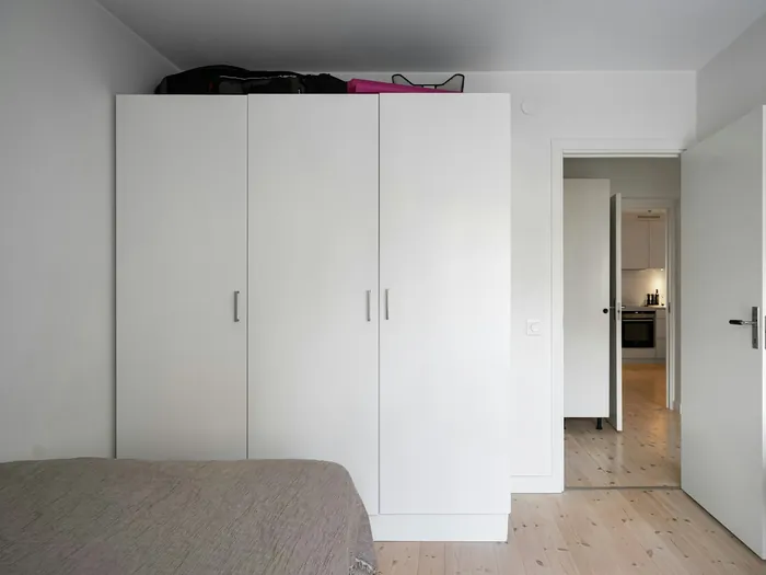 White three-door wardrobe in a bedroom, the doors side by side on one cabinet