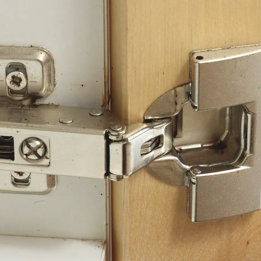 Close-up of a 35 mm concealed cup hinge fitted between a cabinet side and a wooden door